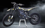 Sur Ron Ultra Bee electric dirt bike on a stand with off-road tires and performance upgrades, shown on a smoky dark background.